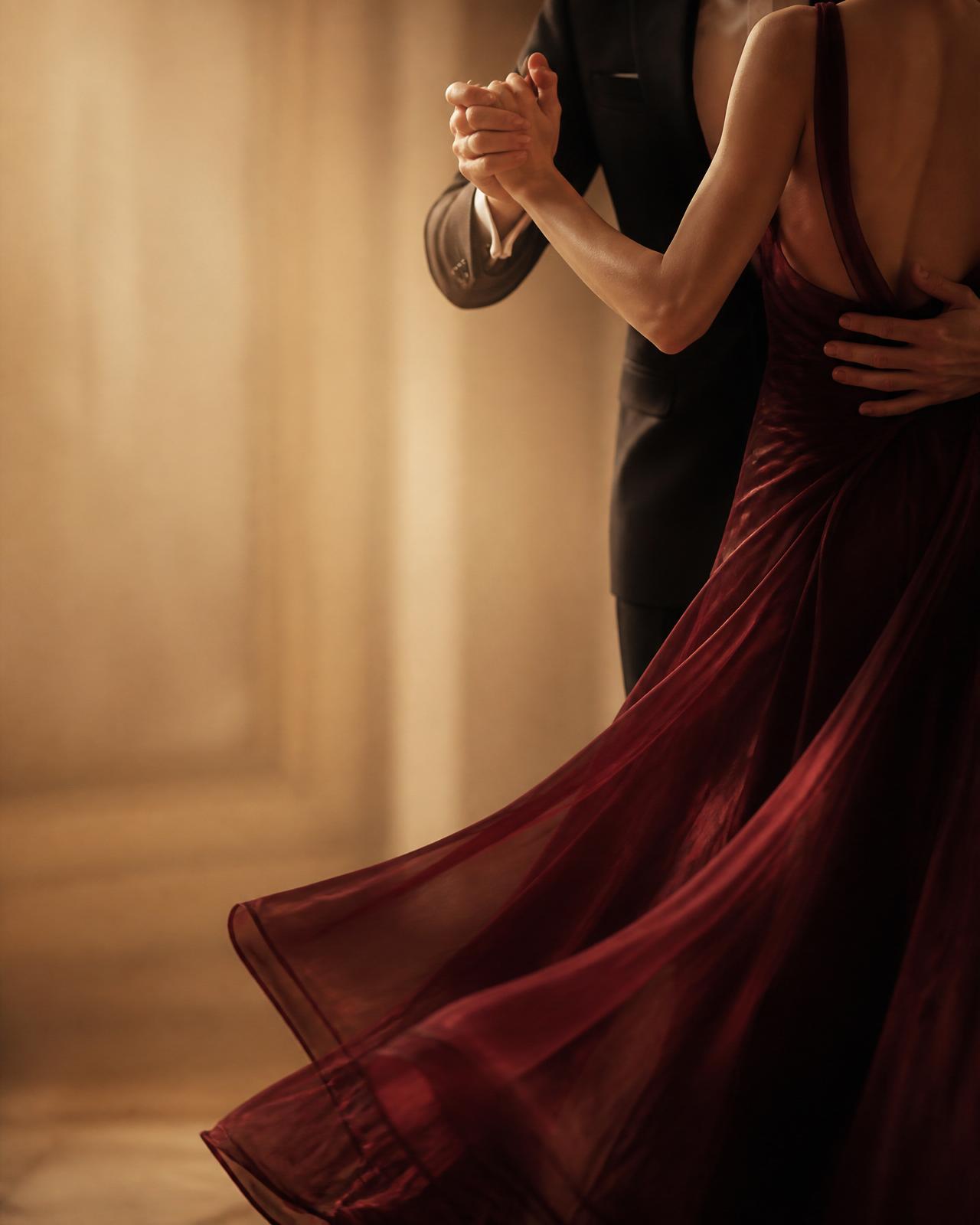 Two partner dancers in warm champagne light, close view of connected hands and flowing burgundy fabric
